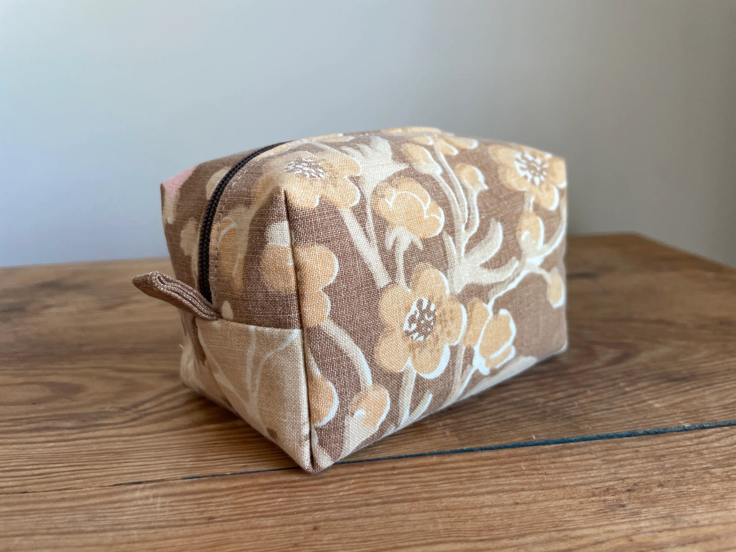 Mini boxnecessär i brun bomull med romantiskt blommönster i rosa, beige, creme och honungsgula toner. Handsydd necessär med rymlig boxform för smink, toalettartiklar, sticktillbehör och annan praktisk förvaring. Det vintageinspirerade blommönstret ger en varm, nostalgisk känsla med lantlig charm.