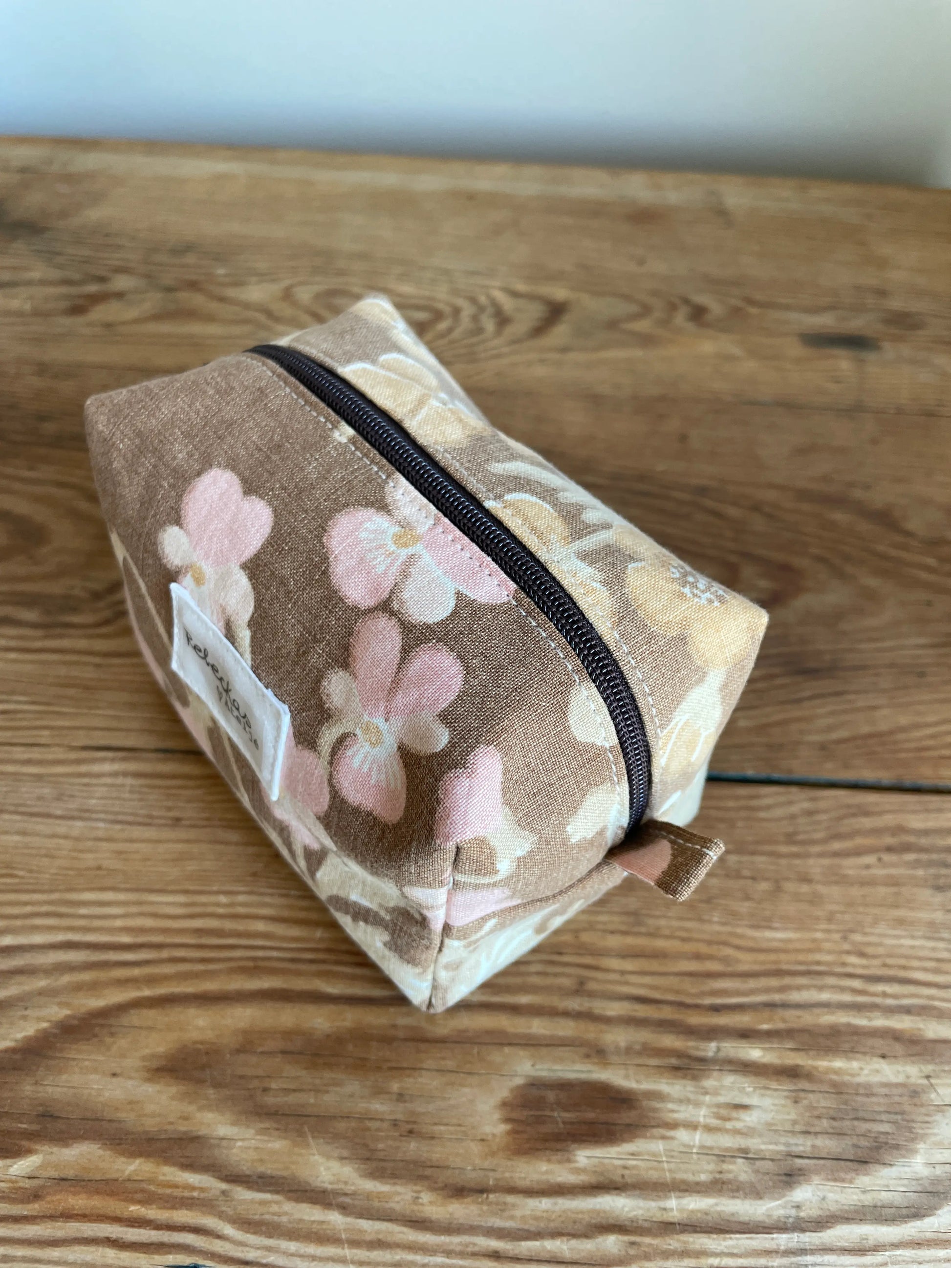 Mini boxnecessär i brun bomull med romantiskt blommönster i rosa, beige, creme och honungsgula toner. Handsydd necessär med rymlig boxform för smink, toalettartiklar, sticktillbehör och annan praktisk förvaring. Det vintageinspirerade blommönstret ger en varm, nostalgisk känsla med lantlig charm.
