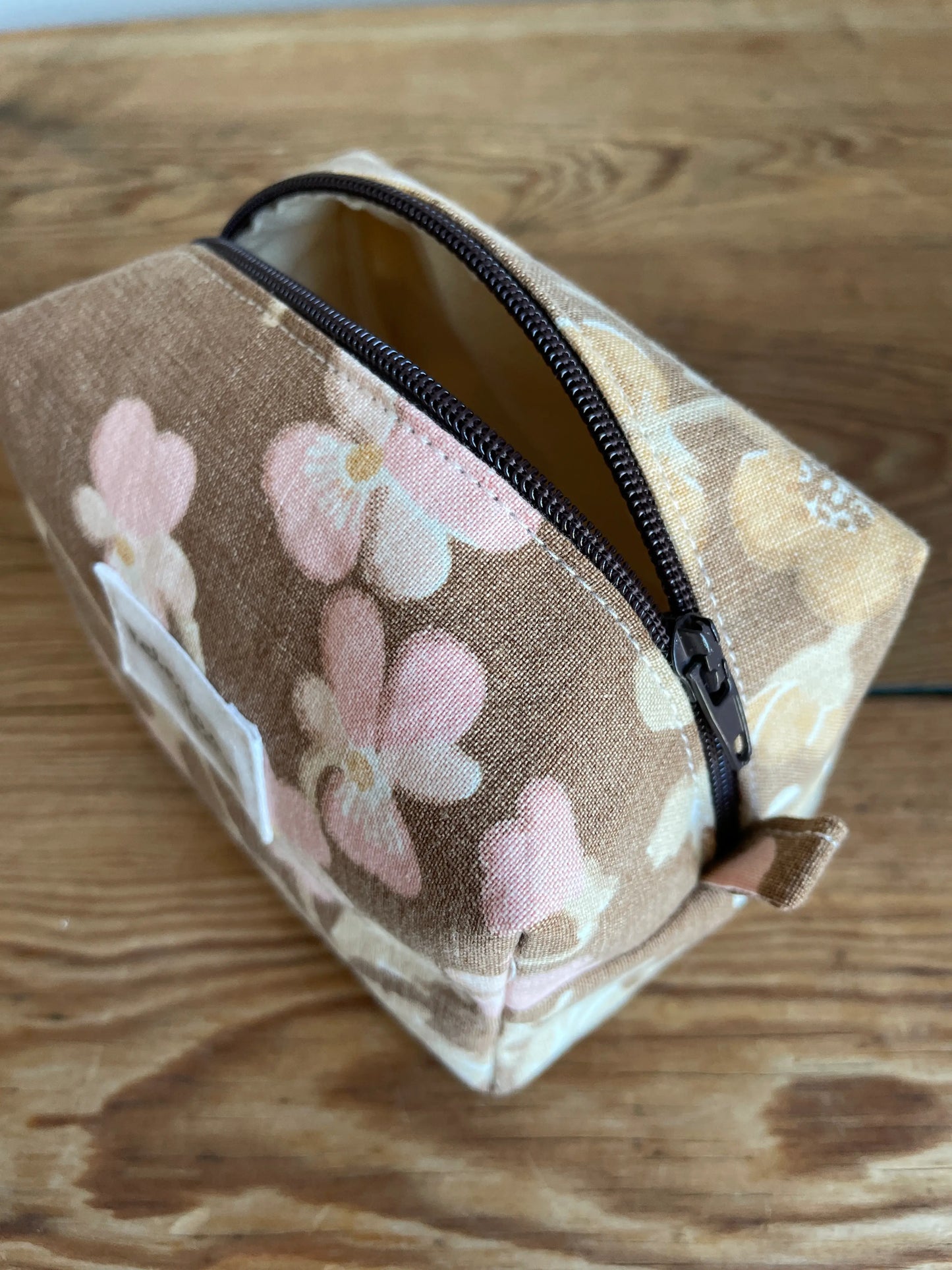 Mini boxnecessär i brun bomull med romantiskt blommönster i rosa, beige, creme och honungsgula toner. Handsydd necessär med rymlig boxform för smink, toalettartiklar, sticktillbehör och annan praktisk förvaring. Det vintageinspirerade blommönstret ger en varm, nostalgisk känsla med lantlig charm.
