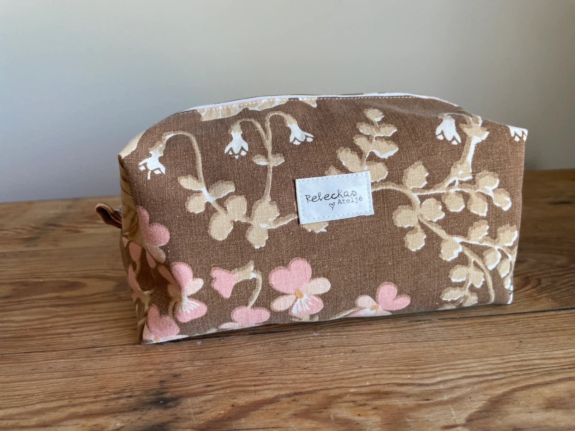 Boxnecessär i brun bomull med romantiskt blommönster i rosa, beige, creme och honungsgula toner. Handsydd necessär med rymlig boxform för smink, toalettartiklar, sticktillbehör och annan praktisk förvaring. Det vintageinspirerade blommönstret ger en varm, nostalgisk känsla med lantlig charm.