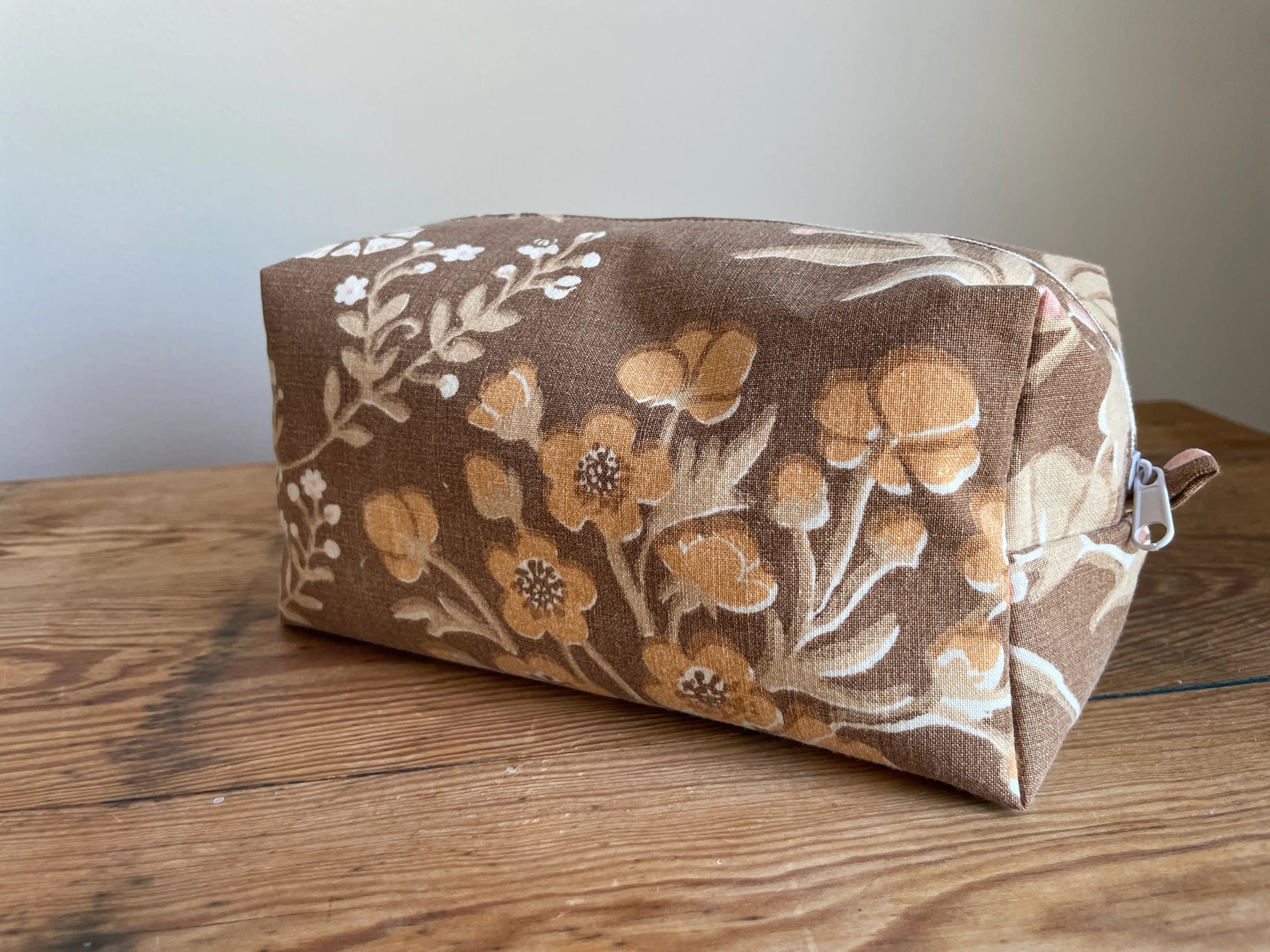Boxnecessär i brun bomull med romantiskt blommönster i rosa, beige, creme och honungsgula toner. Handsydd necessär med rymlig boxform för smink, toalettartiklar, sticktillbehör och annan praktisk förvaring. Det vintageinspirerade blommönstret ger en varm, nostalgisk känsla med lantlig charm.