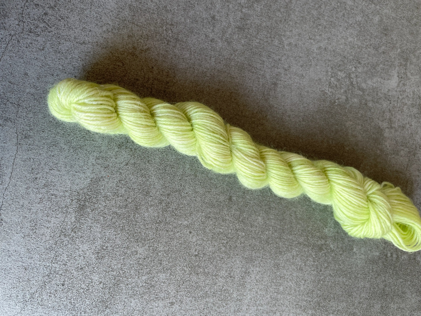 Handfärgat sockgarn-set med 100 g sockgarn i skogsgröna, petrolblå och mossgröna nyanser samt ett 20 g mini-nystan i ljus limegrön kontrastfärg. Garnset för stickade strumpor, sockor och accessoarer där mini-nystanet passar till häl, tå och mudd. Fotograferat på rustikt träbord som framhäver garnets färgskiftningar och glans.
