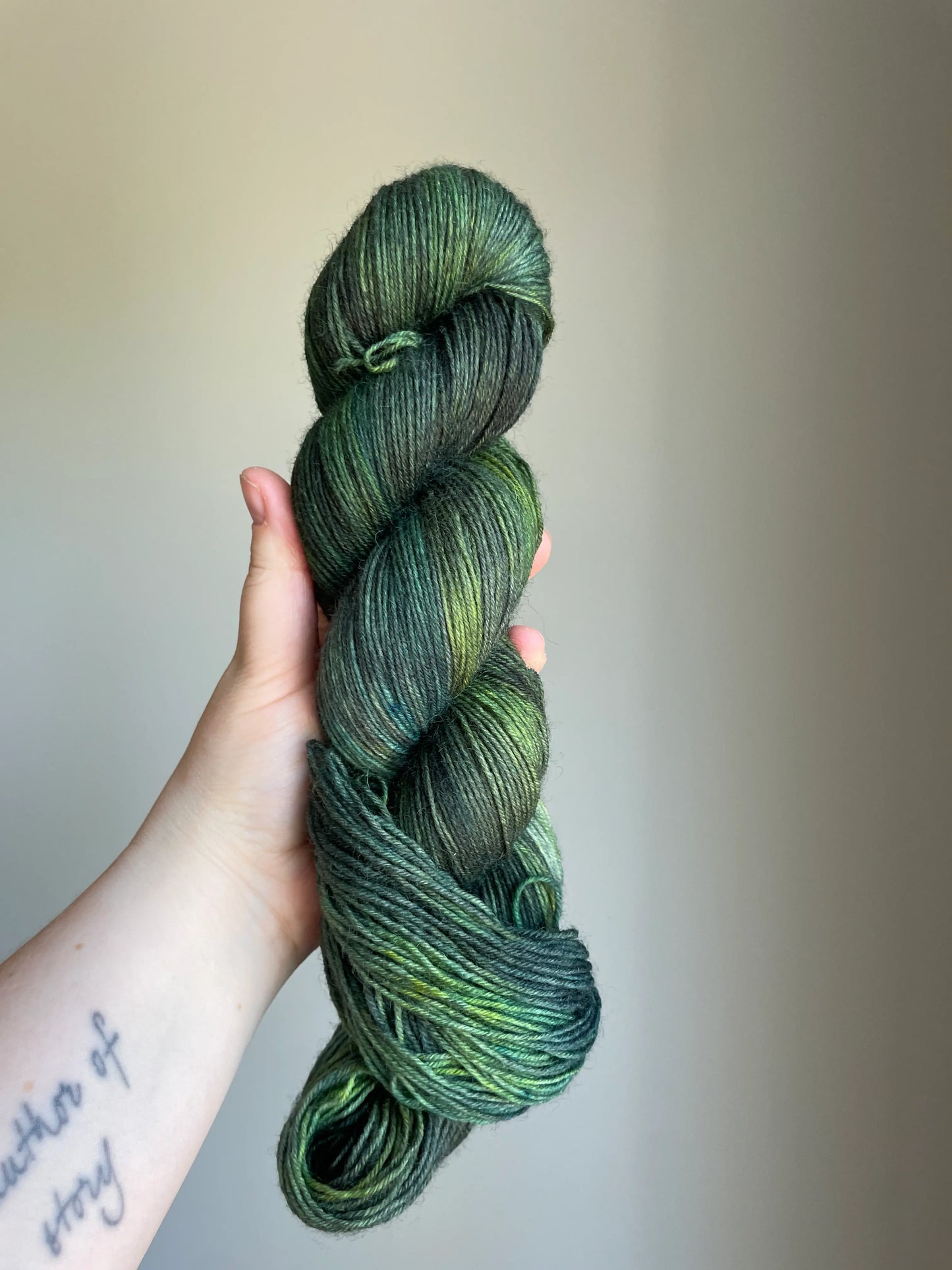 Handfärgat sockgarn-set med 100 g sockgarn i skogsgröna, petrolblå och mossgröna nyanser samt ett 20 g mini-nystan i ljus limegrön kontrastfärg. Garnset för stickade strumpor, sockor och accessoarer där mini-nystanet passar till häl, tå och mudd. Fotograferat på rustikt träbord som framhäver garnets färgskiftningar och glans.
