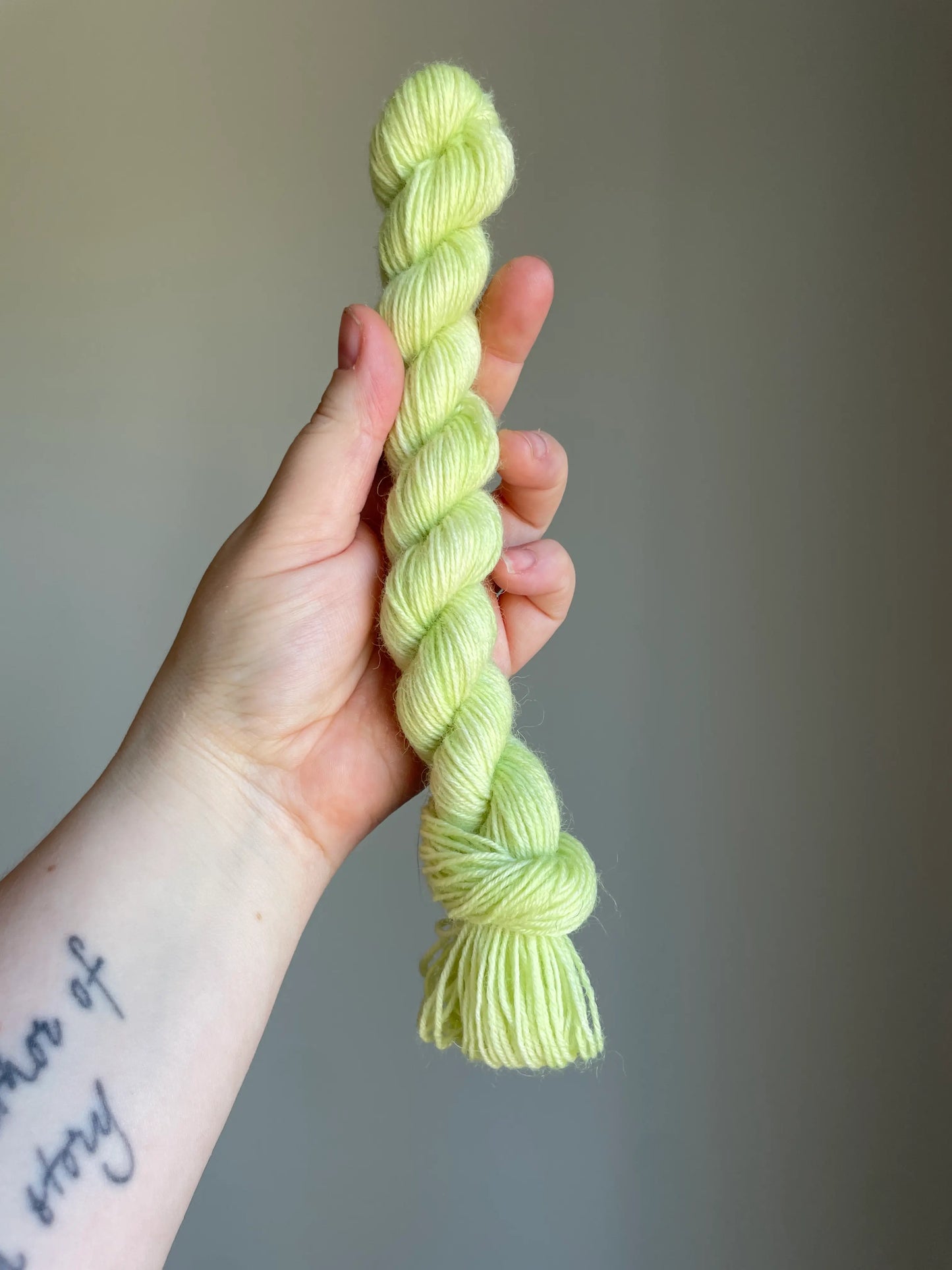 Handfärgat sockgarn-set med 100 g sockgarn i skogsgröna, petrolblå och mossgröna nyanser samt ett 20 g mini-nystan i ljus limegrön kontrastfärg. Garnset för stickade strumpor, sockor och accessoarer där mini-nystanet passar till häl, tå och mudd. Fotograferat på rustikt träbord som framhäver garnets färgskiftningar och glans.